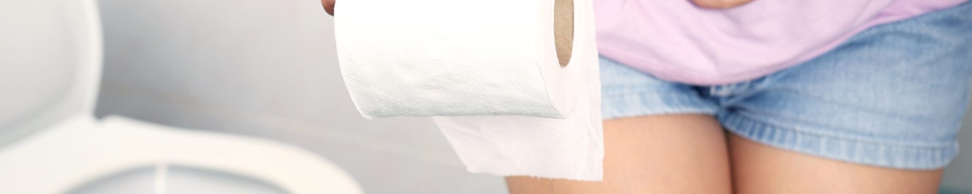 A woman wearing a pink shirt carries toilet paper to the toilet.